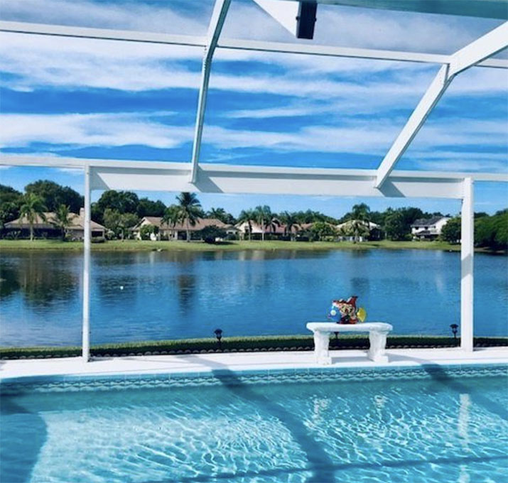 A photo of a new lanai enclosure installation with a view of the pool and surrounding landscaping in Florida